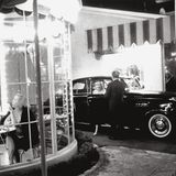 Blick in ein rundes Café, hinter dem eine Frau aus einem Rolls-Royce steigt