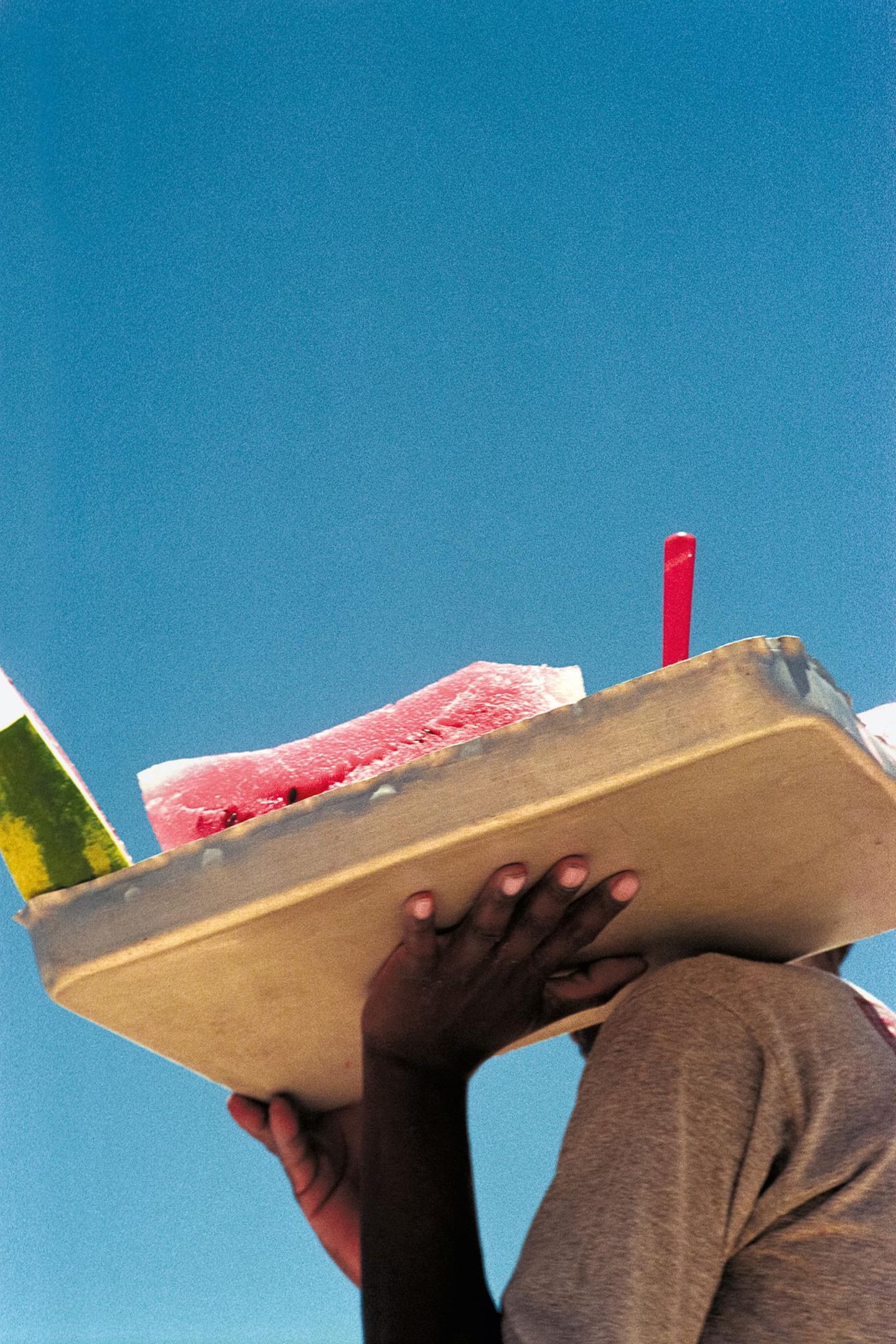 Eine schwarze Hand trägt ein Tablett mit geschnittener Wassermelone