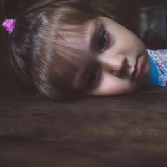 Kinder: Ein kleines Mädchen legt traurig ihren Kopf auf den Tisch