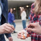 Vor einer Schule nehmen sich Schüler Zigaretten aus einer Päckchen