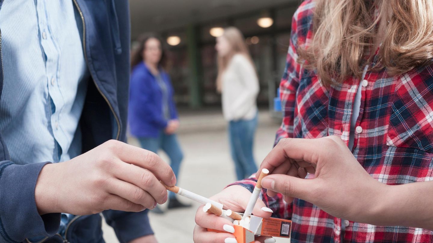 Vor einer Schule nehmen sich Schüler Zigaretten aus einer Päckchen