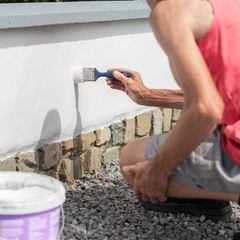 eine Person streicht eine Hausfassade weiß
