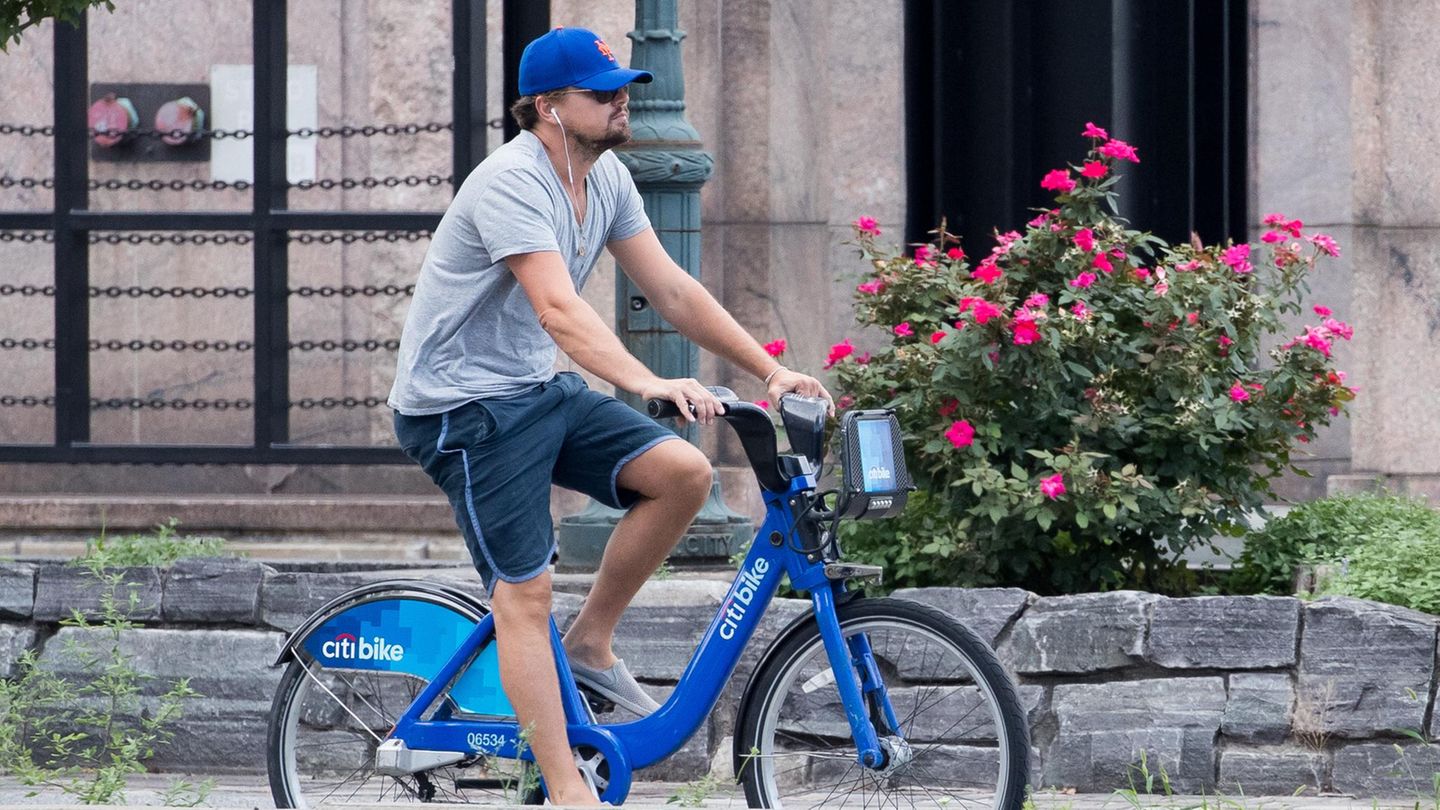 Leonardo diCaprio privat auf einem Stadtrad, E-Bike. Er trägt eine blaue Kappe