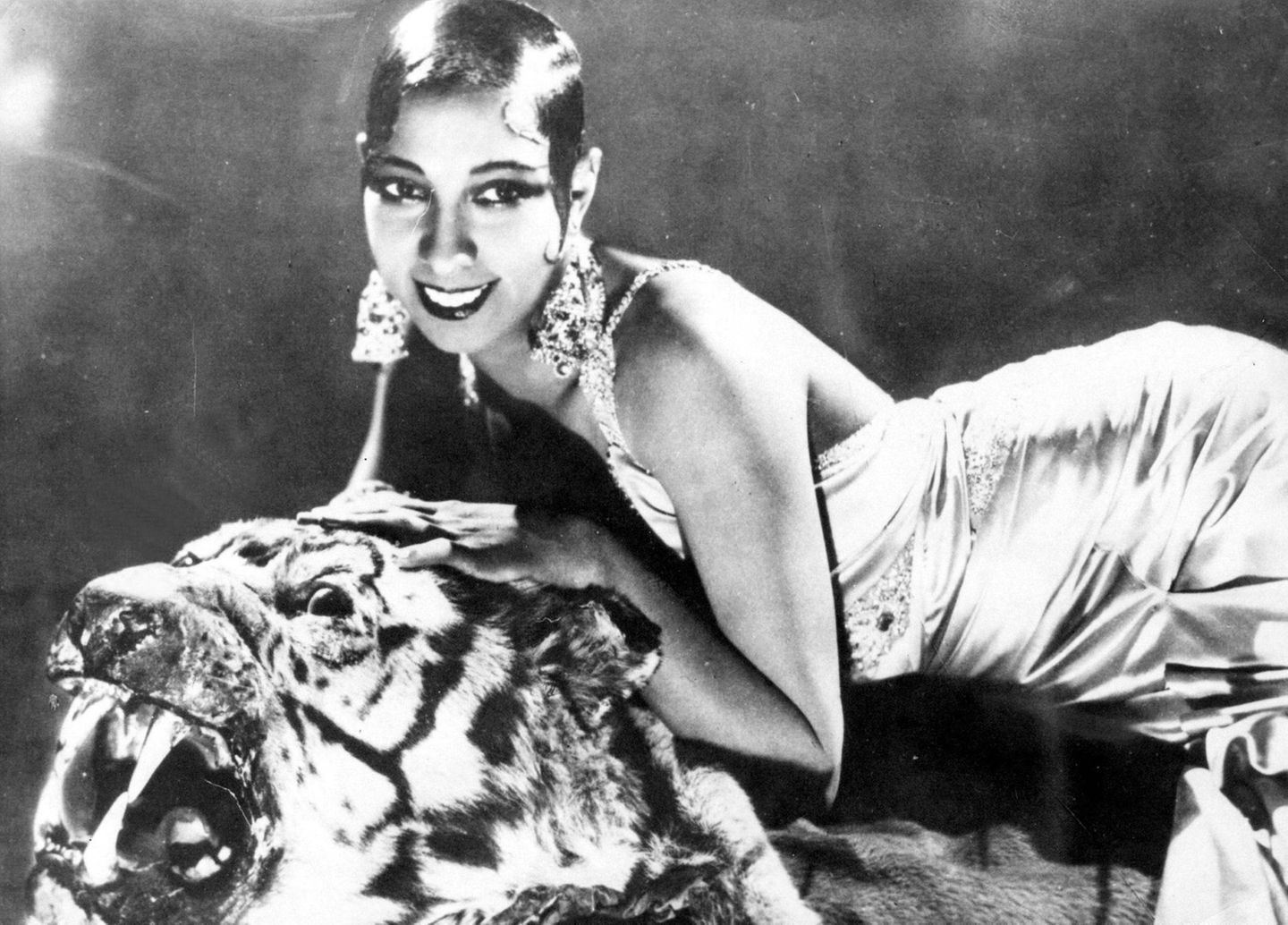 Josephine Baker liegt auf einem Tigerfell und trägt große Ohrringe