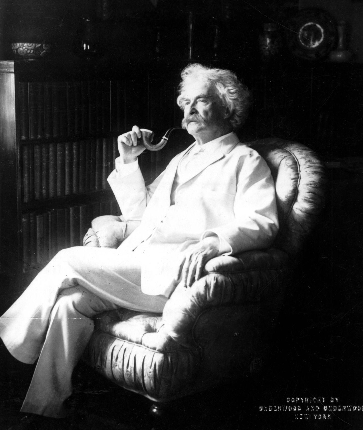 Mark Twain mit Pfeife und weißem Anzug in einem Sessel.