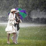 Zwei Damen unter Schirmen laufen durch strömenden Regen