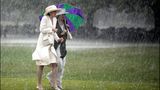 Zwei Damen unter Schirmen laufen durch strömenden Regen
