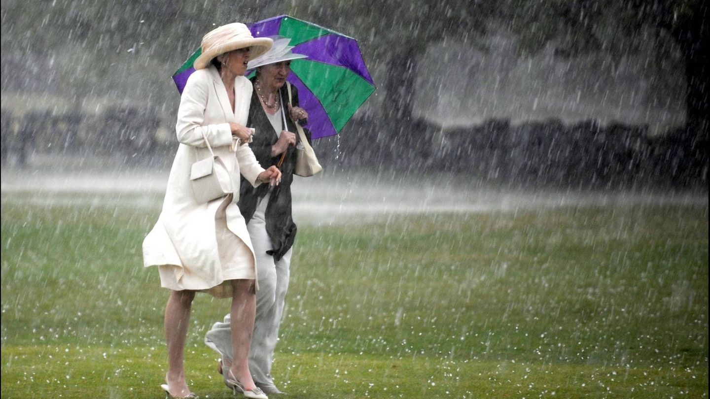 Zwei Damen unter Schirmen laufen durch strömenden Regen