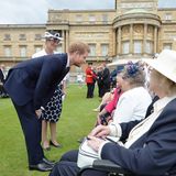 Prinz Harry im dunklen Anzug beugt sich zu älteren Damen im Rollstuhl herunter, mit denen er plaudert