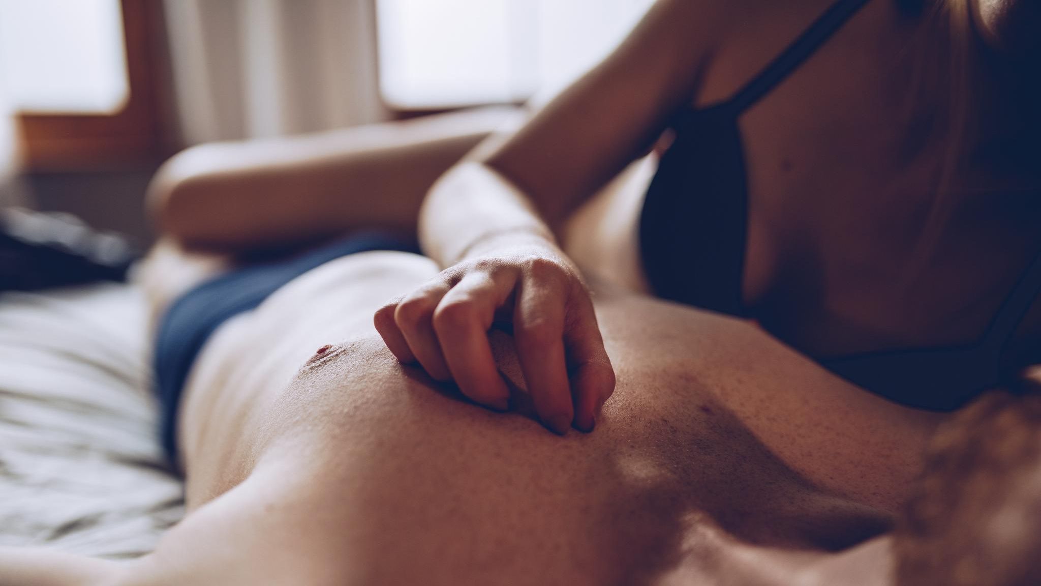 Escort: Eine Frau in BH liegt auf einem Mann in Shorts