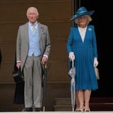 König Charles im grauen Frack und Camilla im blauen Kostüm treten aus dem Buckingham Palast in den Garten