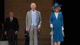 König Charles im grauen Frack und Camilla im blauen Kostüm treten aus dem Buckingham Palast in den Garten