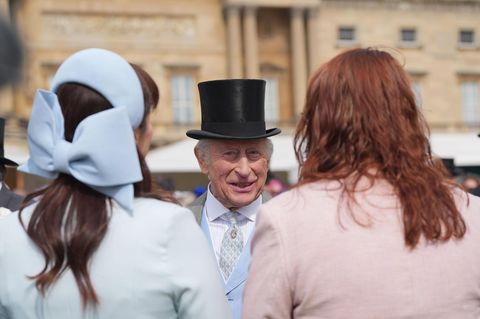 König Charles mit schwarzem Zylinder im Gespräch mit zwei Frauen aus dem Volk