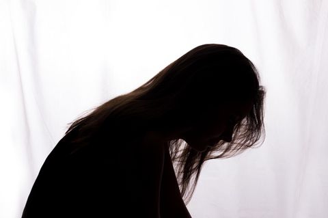 Eine Frau sitzt mit hängendem Kopf vor einem weißen Hintergrund.