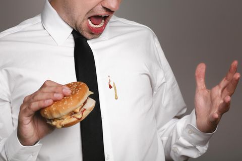 Ein Mann kleckert beim Essen auf sein Hemd