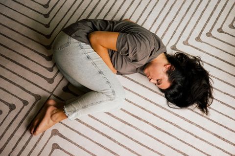 Thema Long Covid: Frau liegt sich krümmend auf dem Boden