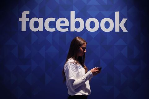 Eine Frau steht vor einem Logo der Meta-Tochter Facebook