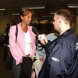 Naddel gibt am Flughafen ein Interview, sie trägt einen rosafarbenen Blazer und spricht in ein Mikrofon