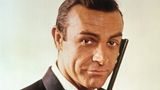Sean Connery als James Bond im Portrait. Sein Blick ist lässig, mit der Hand hält er eine Waffe an sein Gesicht