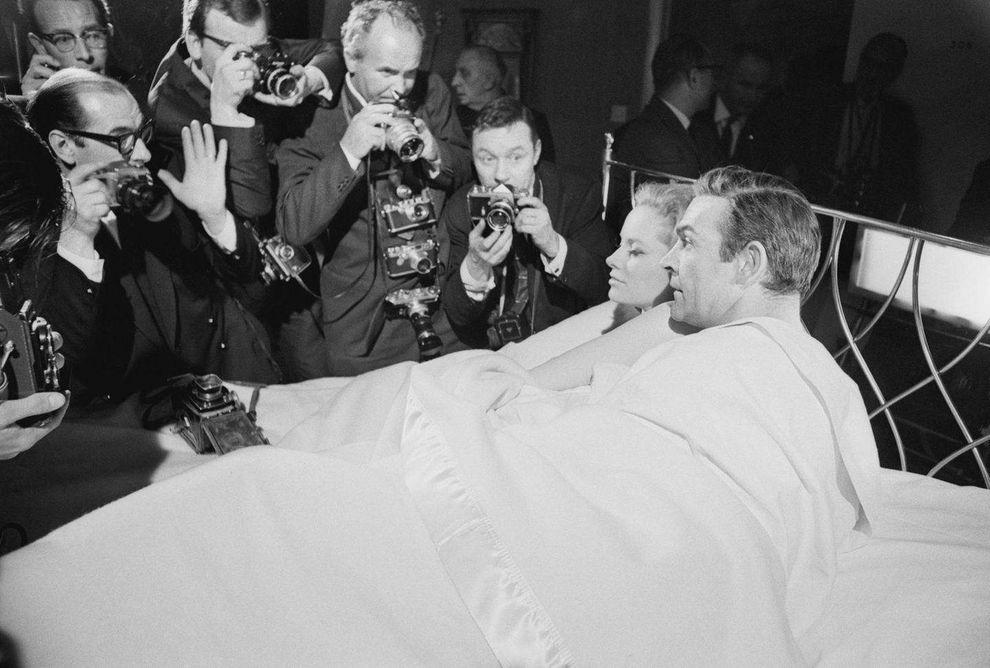 Sean Connery liegt für eine Szene mit einer Frau im Bett. Um ihn herum stehen Fotografen, die am Set zuschauen
