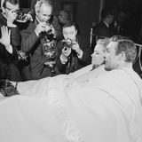 Sean Connery liegt für eine Szene mit einer Frau im Bett. Um ihn herum stehen Fotografen, die am Set zuschauen
