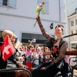 Zoë Më auf einem Wagen in Tracht und mit Blumen in der Hand