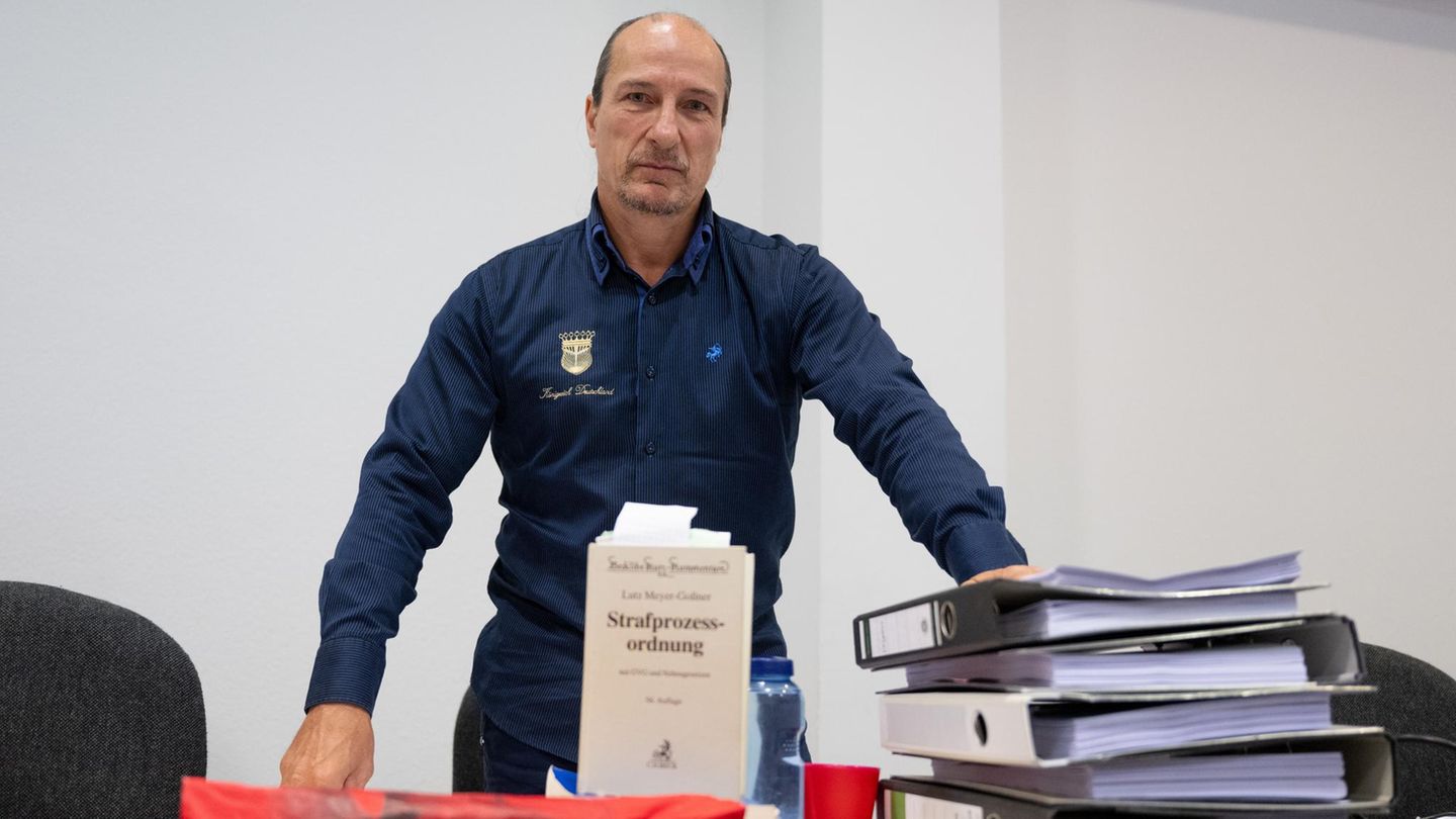 Peter Fitzek steht in einem Gerichtssaal, vor ihm eine Strafprozessordnung