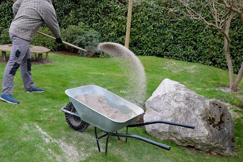 Rasen sanden: Nach dem Beschneiden des Rasens trägt ein Gärtner weißen Quarzsand auf