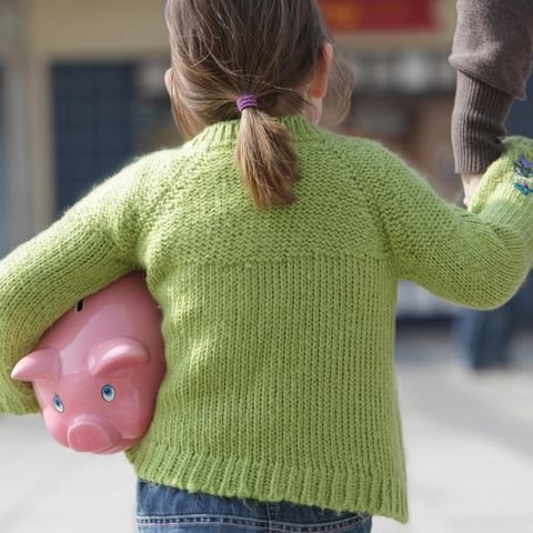 Ein kleines Mädchen trägt ein Sparschwein unter dem Arm