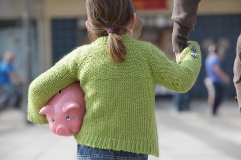 Ein kleines Mädchen trägt ein Sparschwein unter dem Arm