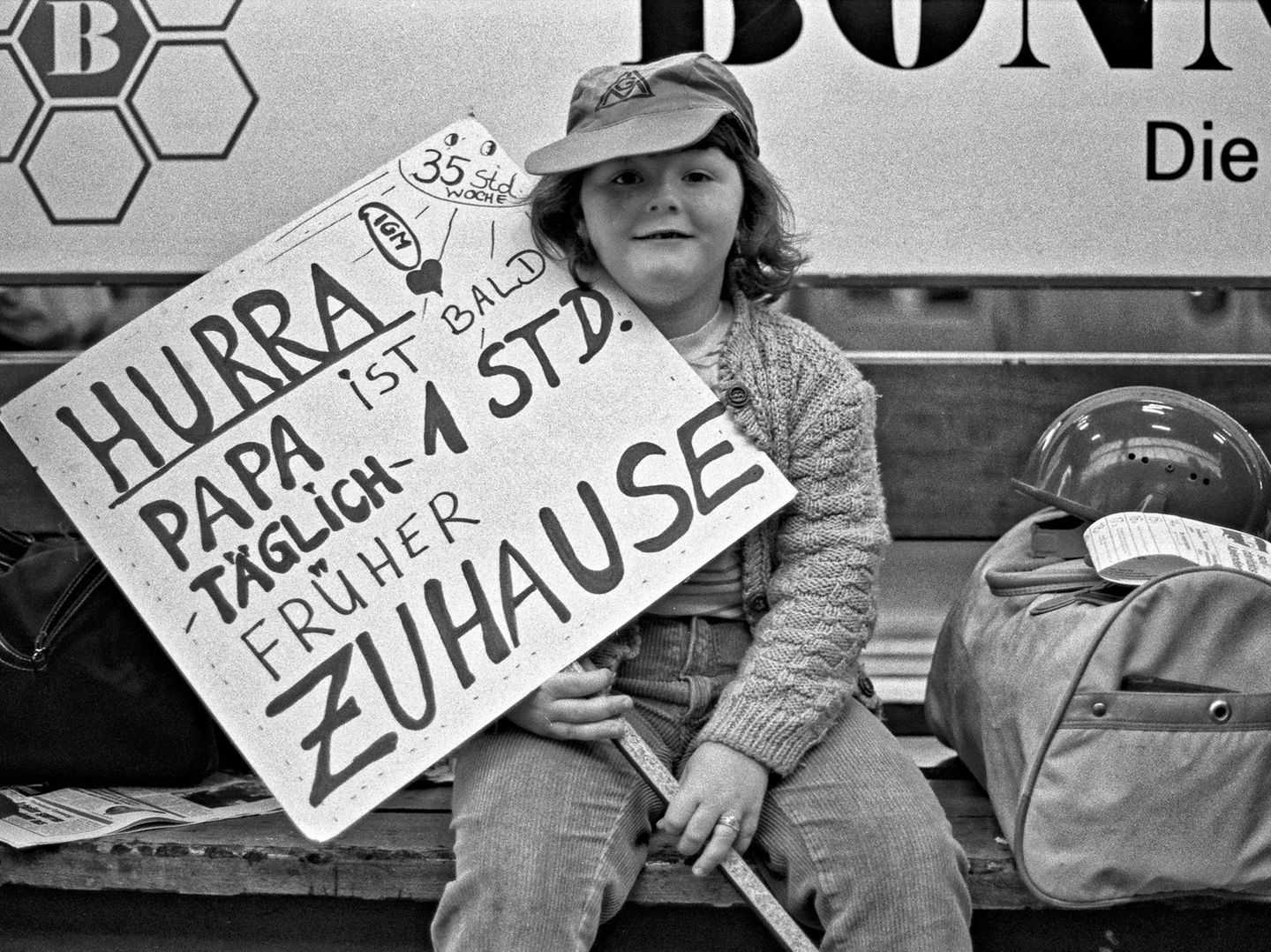 Kind mit Plakat "Hurra, Papa ist bald eine Stunde früher zu Hause"