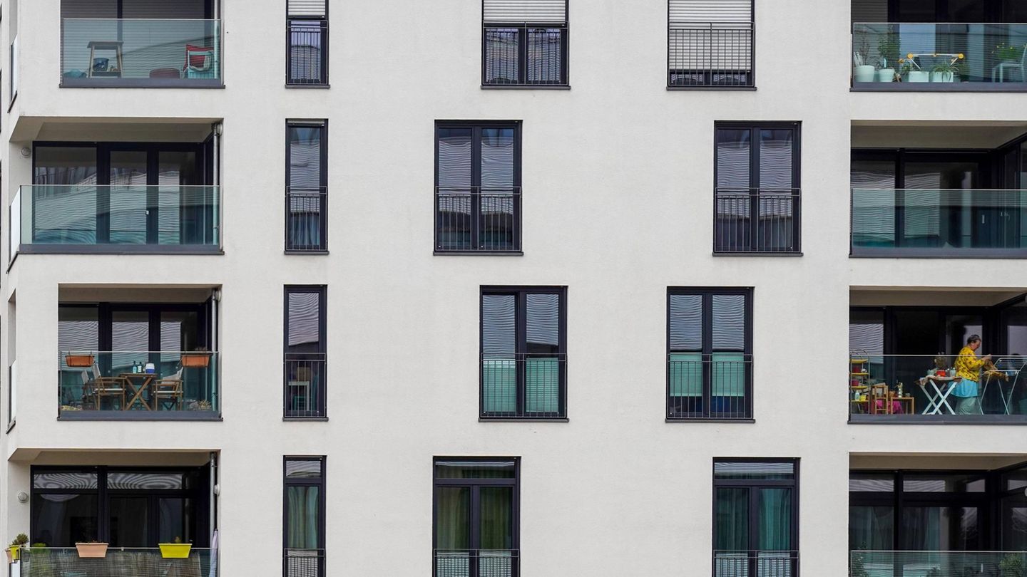 Frau hängt Wäsche auf ihrem Balkon in einem modernen Mehrfamilienhaus auf