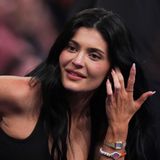 Kylie Jenner sitzt im schwarzen Top in der ersten Reihe und schaut aufs Feld