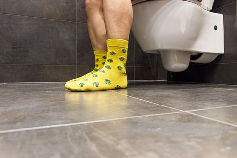 Ein Mann mit bunten Socken, sitzt auf einer Toilette