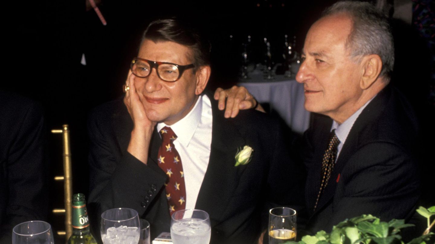 Yves Saint Laurent und sein Freund Pierre Bergé sitzen an einem Tisch. Er stützt seinen Kopf auf die Hand