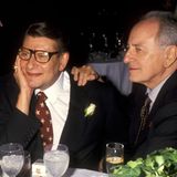 Yves Saint Laurent und sein Freund Pierre Bergé sitzen an einem Tisch. Er stützt seinen Kopf auf die Hand
