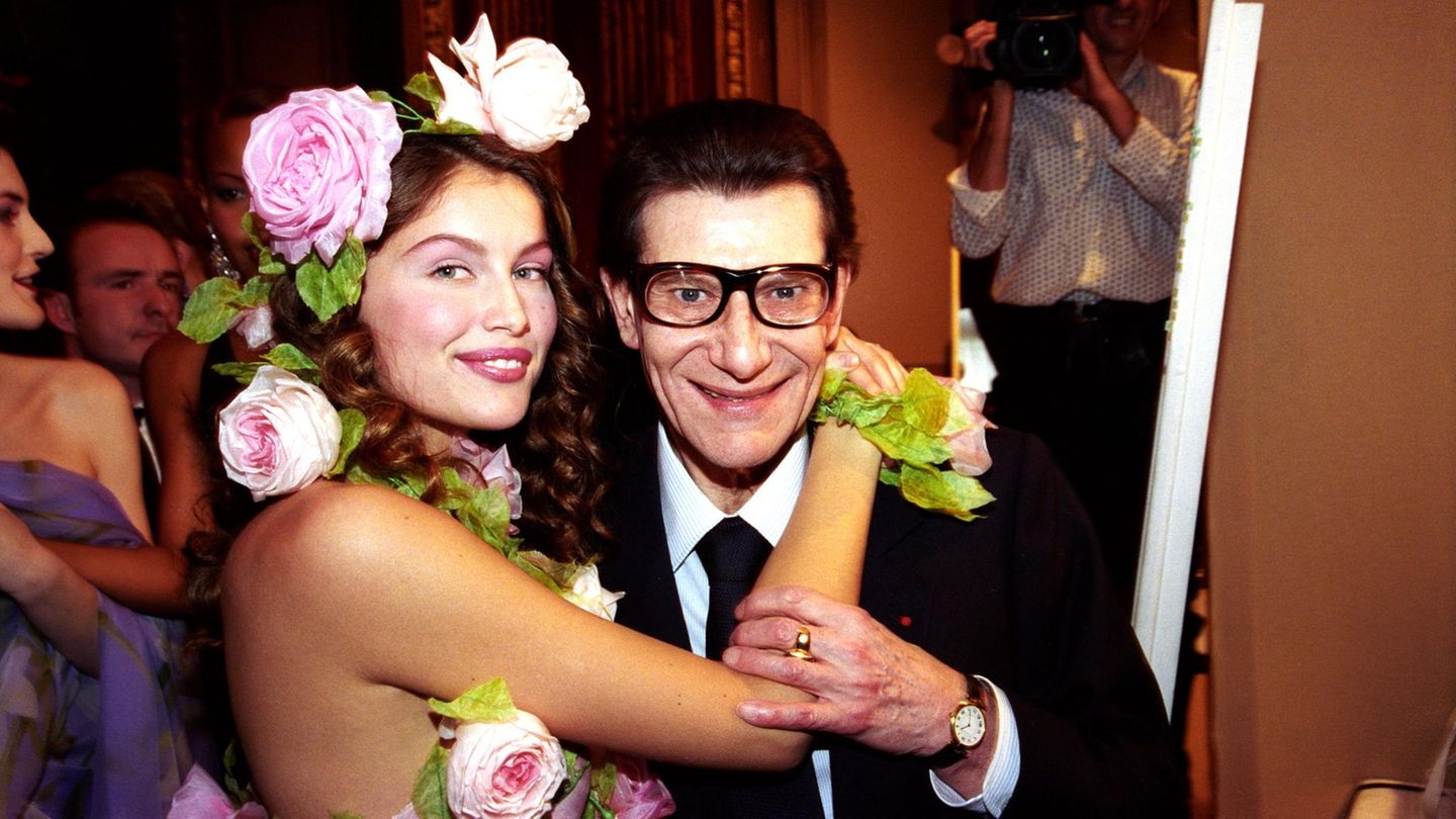 Das Model Laetizia Casta umarmt Yves Saint Laurent, der eine Brille mit dunklem Rahmen trägt