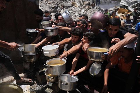 Eine Menschengruppe streckt Helfern bei der Essensverteilung in Gaza leere Töpfe entgegen