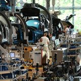 An der Montagelinie arbeiten weißgekleidete Monteure an an Kränen schwebenden ID.3-Karosserien im Volkswagenwerk in Dresden