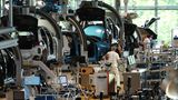 An der Montagelinie arbeiten weißgekleidete Monteure an an Kränen schwebenden ID.3-Karosserien im Volkswagenwerk in Dresden