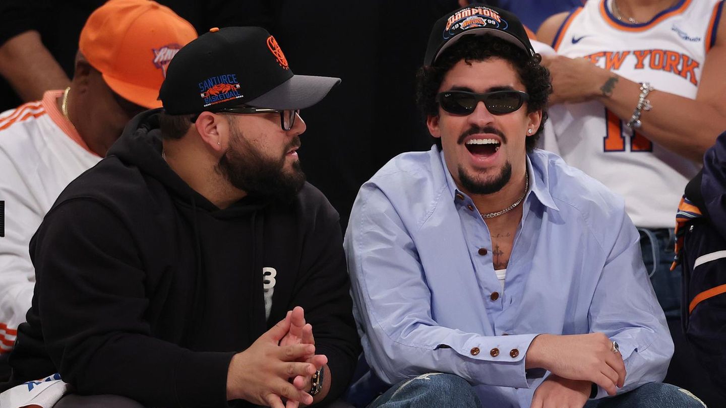 Der Rapper Bad Bunny sitzt mit schwarzer Sonnenbrille und New York Knicks-Cap in der ersten Reihe