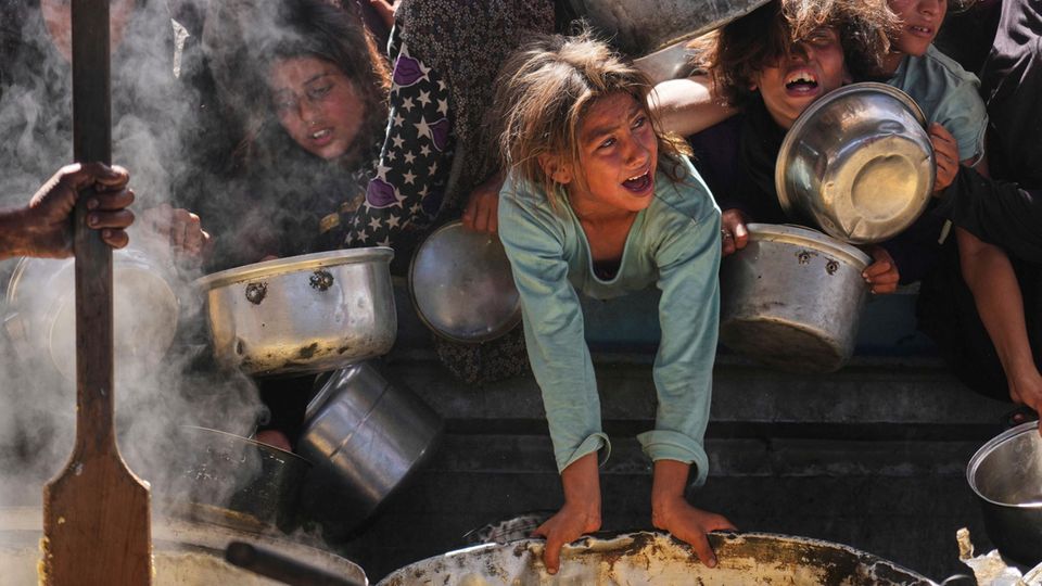 Humans in Gaza waiting for food with bowls, child in the foreground, desperate faces