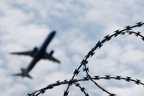 Ein Flugzeug hebt am Flughafen BER hinter einem Zaun mit Natodraht ab: Trumps Abschiebepolitik