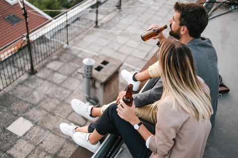 Dealnews: Junges Pärchen sitzt mit Sneakern und Bier auf einem Hausdach