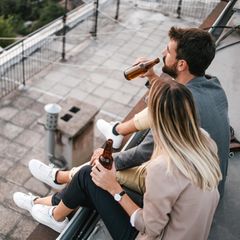 Dealnews: Junges Pärchen sitzt mit Sneakern und Bier auf einem Hausdach