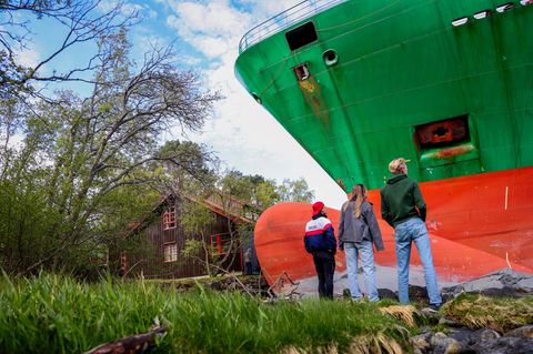 Drei Menschen stehen in Norwegen am Bug eines Containerschiffes, das ihren Garten gerammt hat und wirken klein