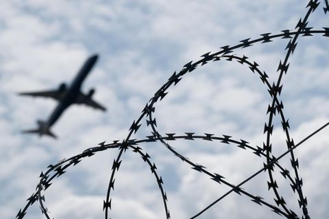 Ein Flugzeug hebt am Flughafen BER hinter einem Zaun mit Natodraht ab