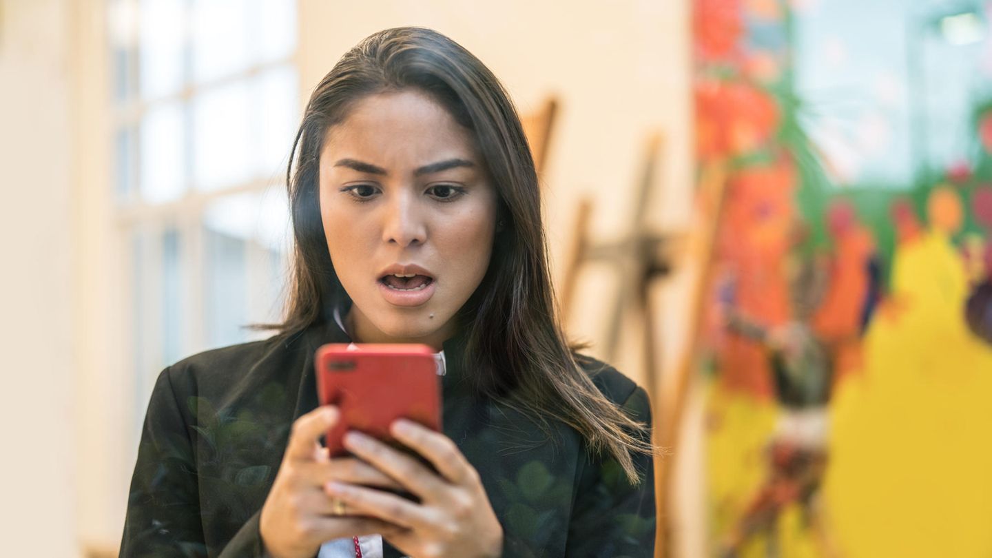 Eine junge Frau schaut erstaunt auf ihr iPhone