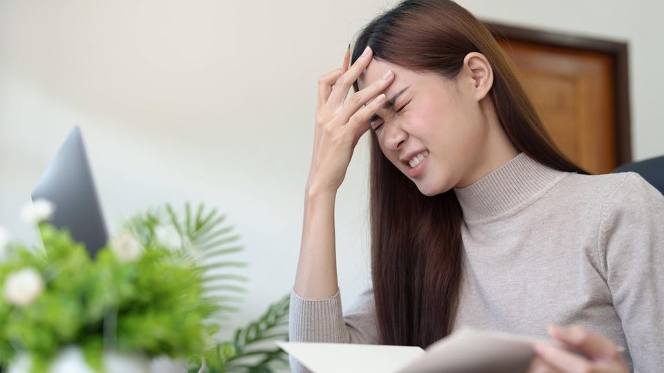 Eine Frau sitzt am Schreibtisch, blättert in einem Buch und denkt angestrengt nach