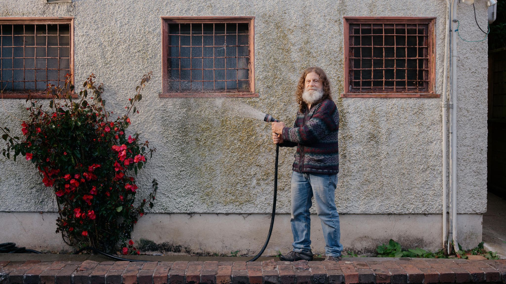 Neurowissenschaftler Robert M. Sapolsky wässert eine Gartenpflanze vor einer Hausfassade